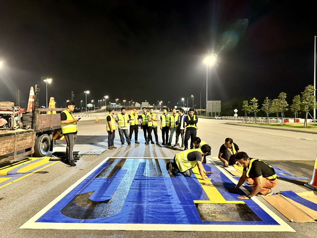 Workers assembling large BUS lettering on a coloured road area